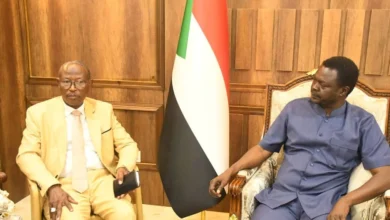 لقاء بين مسؤولين أمام العلم السوداني
