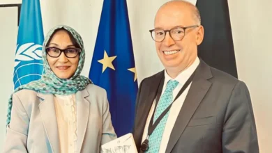 سفيرة السودان ومسؤول ألماني أمام أعلام ألمانيا والاتحاد الأوروبي والأمم المتحدة