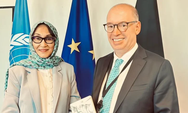 سفيرة السودان ومسؤول ألماني أمام أعلام ألمانيا والاتحاد الأوروبي والأمم المتحدة